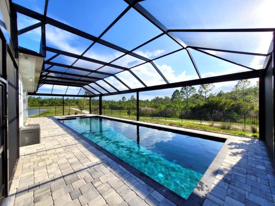There is a swimming pool in the backyard of a house with a screened in area.