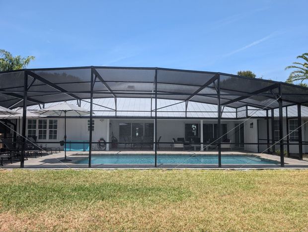 There is a swimming pool in the backyard with a screened in area.