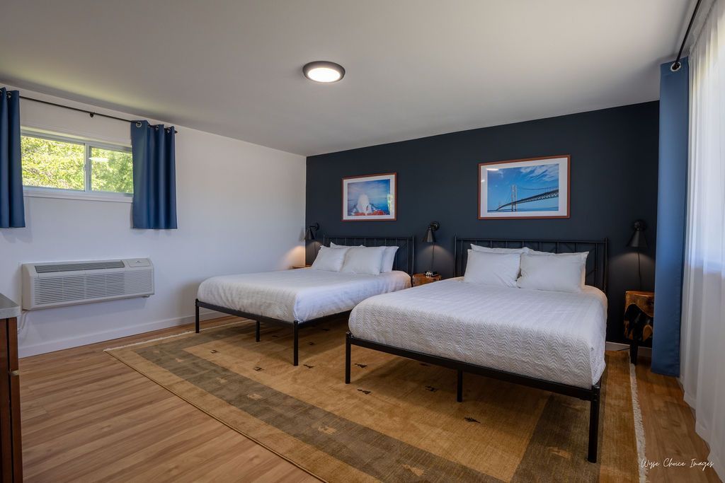 A hotel room with two queen beds, a window with blue curtains, and a dark blue accent wall.