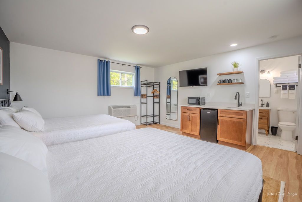 Studio apartment with two beds, kitchenette, and bathroom. White walls, wooden cabinets, and flooring.