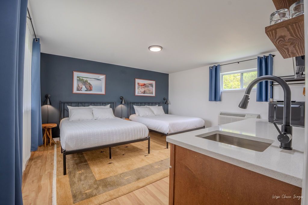 Studio apartment with two beds, kitchenette, and blue accent wall.
