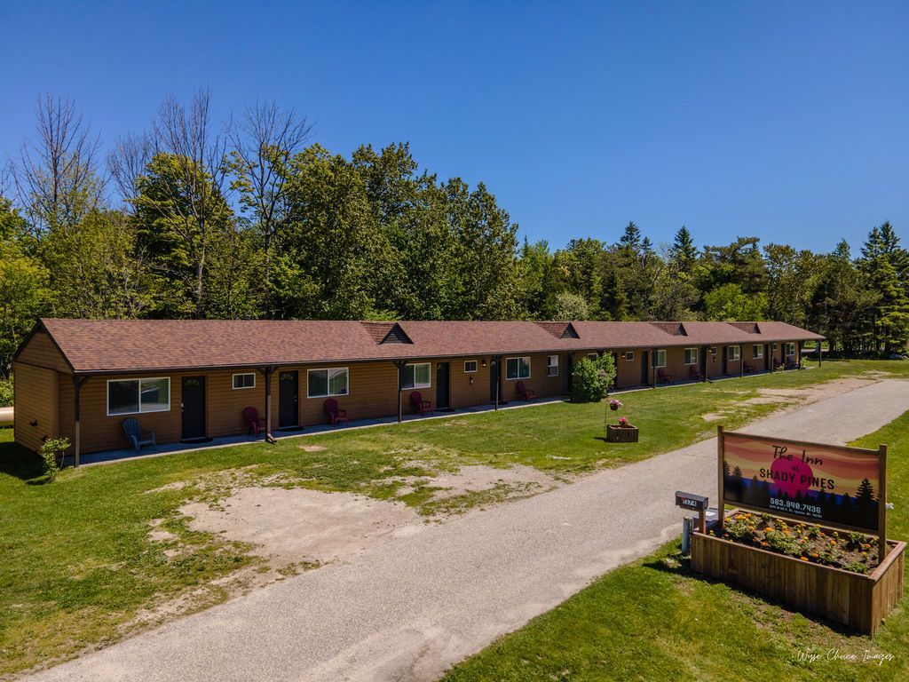 Motel with brown roof and beige walls, sign with a pink creature, gravel driveway, and green lawn.