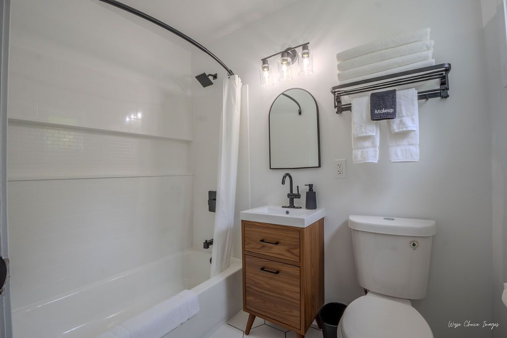 White bathroom with a shower, vanity, toilet, and towel rack; black fixtures, wood vanity.