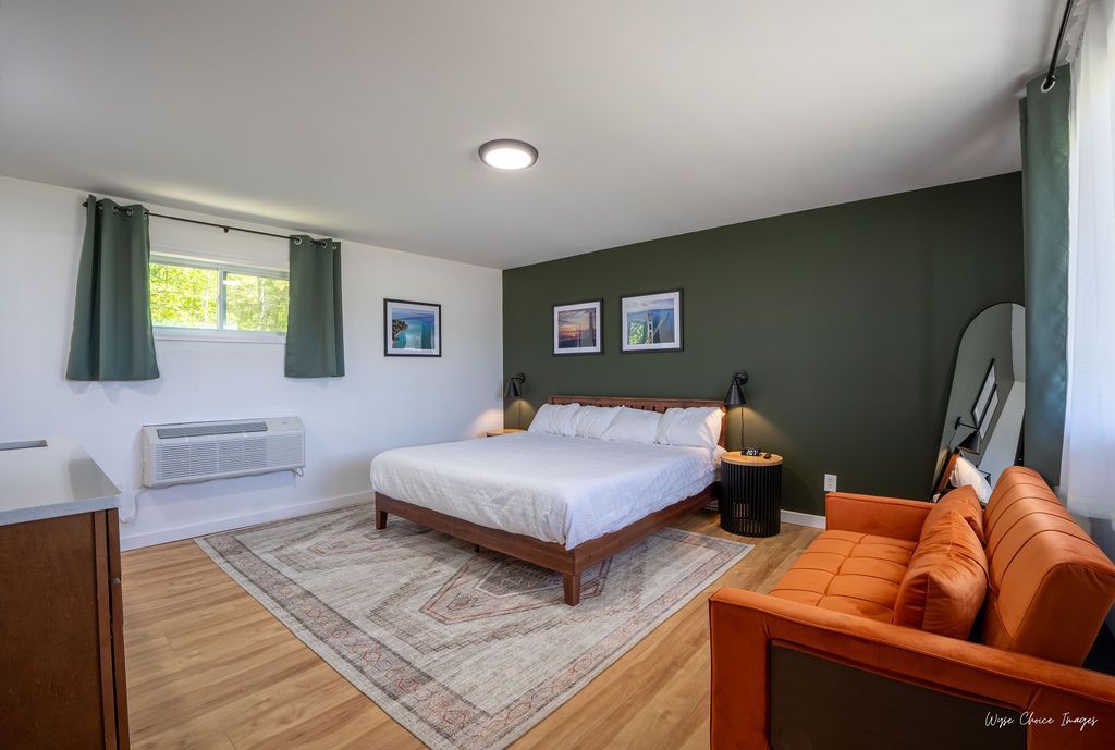 Bedroom with green accent wall, bed, orange couch, wood floor, rug, surfboard.