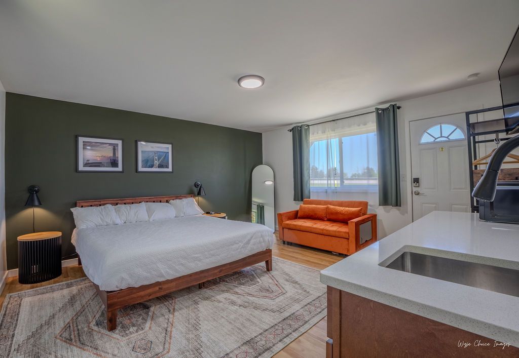 Cozy studio apartment with a bed, orange sofa, kitchen, and dark green accent wall.