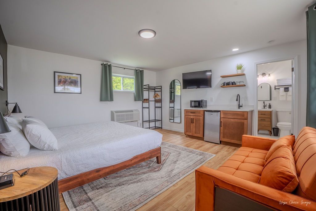 Studio apartment with bed, orange couch, kitchenette, and mirror.