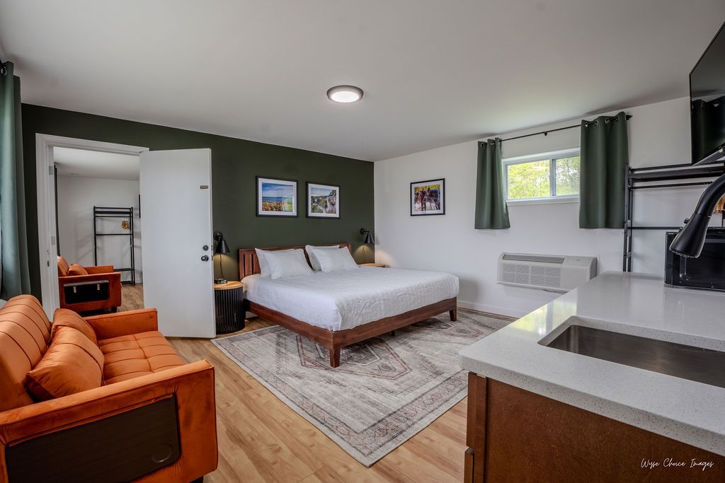Studio apartment with bed, orange couch, kitchen area, and doorway to a second room with bunk beds.