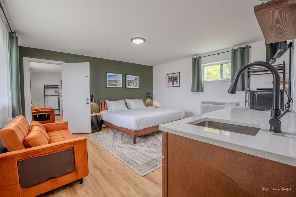Studio apartment interior: bed, orange couch, kitchen area, wood floors, green accent wall, white walls.