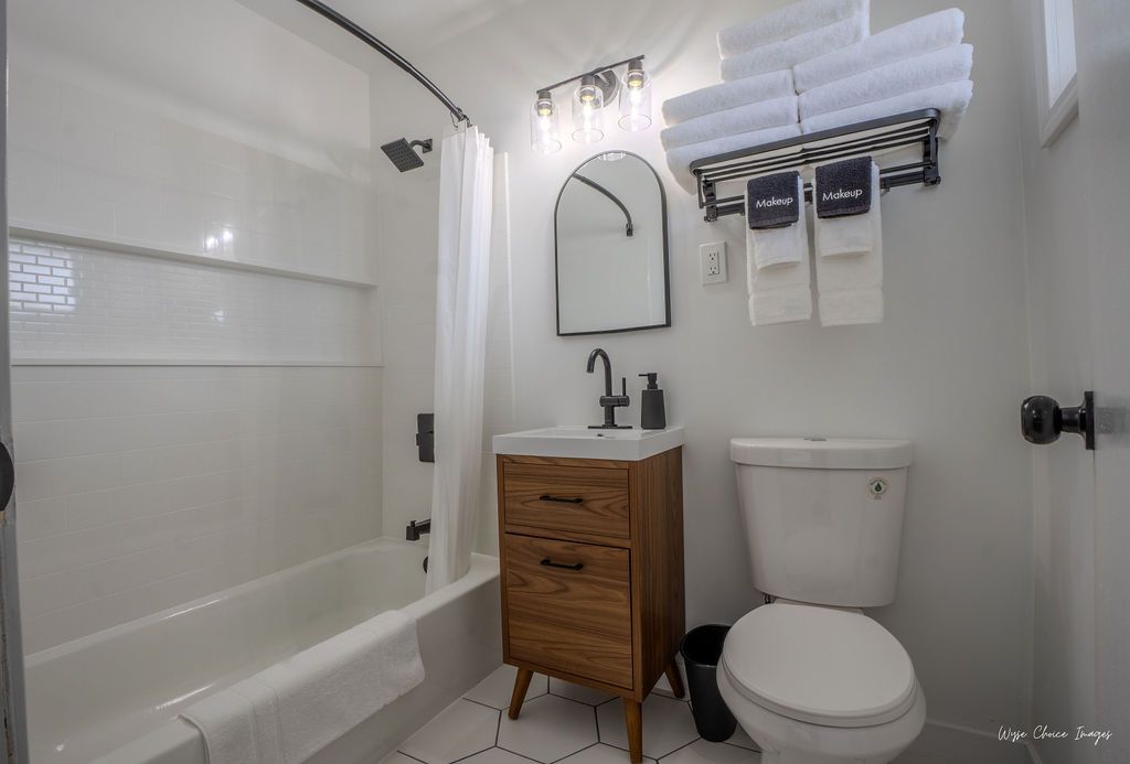 Bathroom with a white tub and toilet, wooden vanity, black fixtures, and a towel rack with clean white towels.