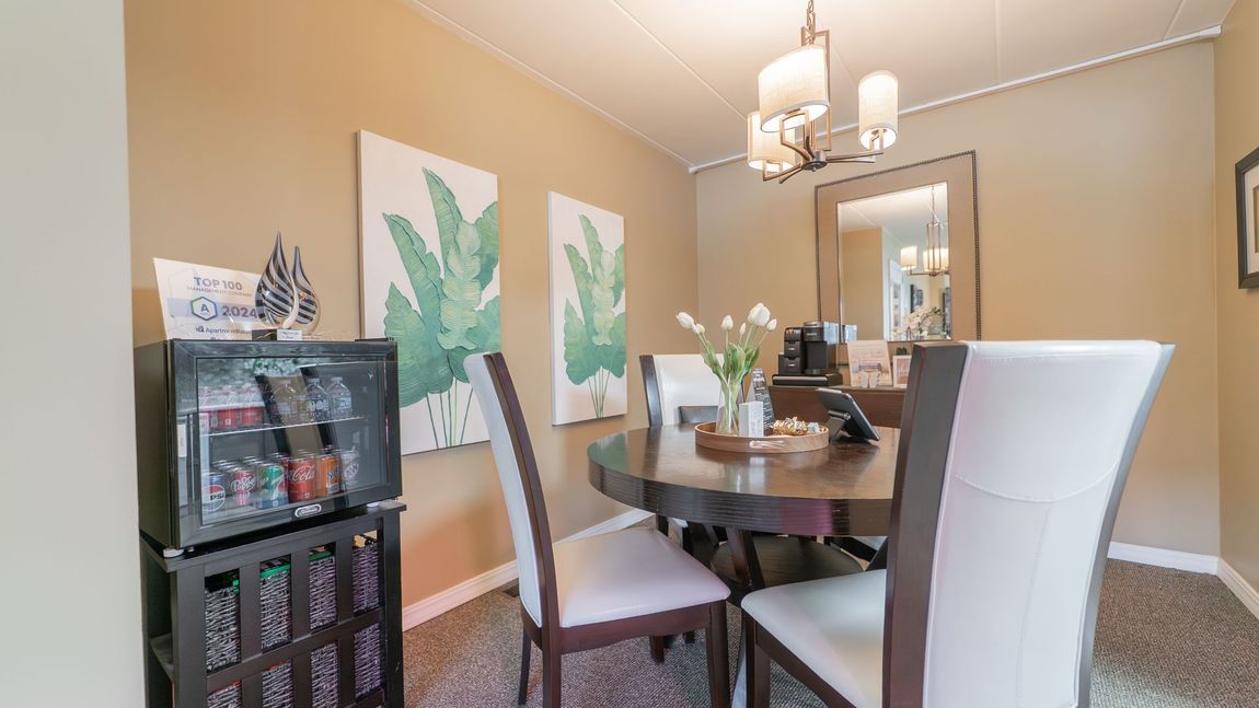 Dining room with round table, white chairs, and artwork on tan walls.
