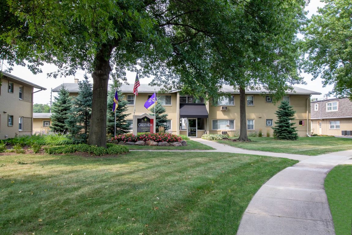 Apartment complex courtyard with trees, lawn, flower beds, and a curved sidewalk