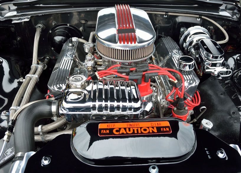 Customized car engine bay with chrome parts, red spark plug wires, and CAUTION fan cover