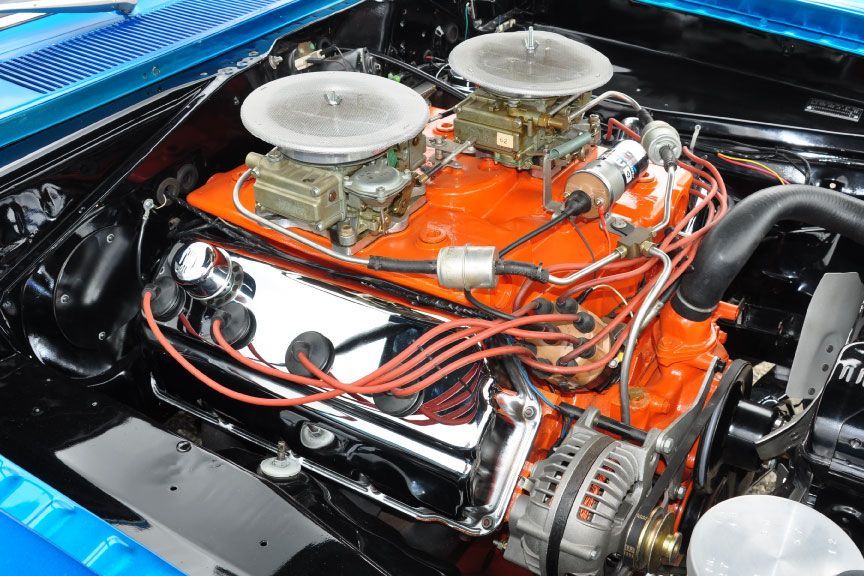 Classic car engine bay with bright orange V8 and dual carburetors under a blue hood