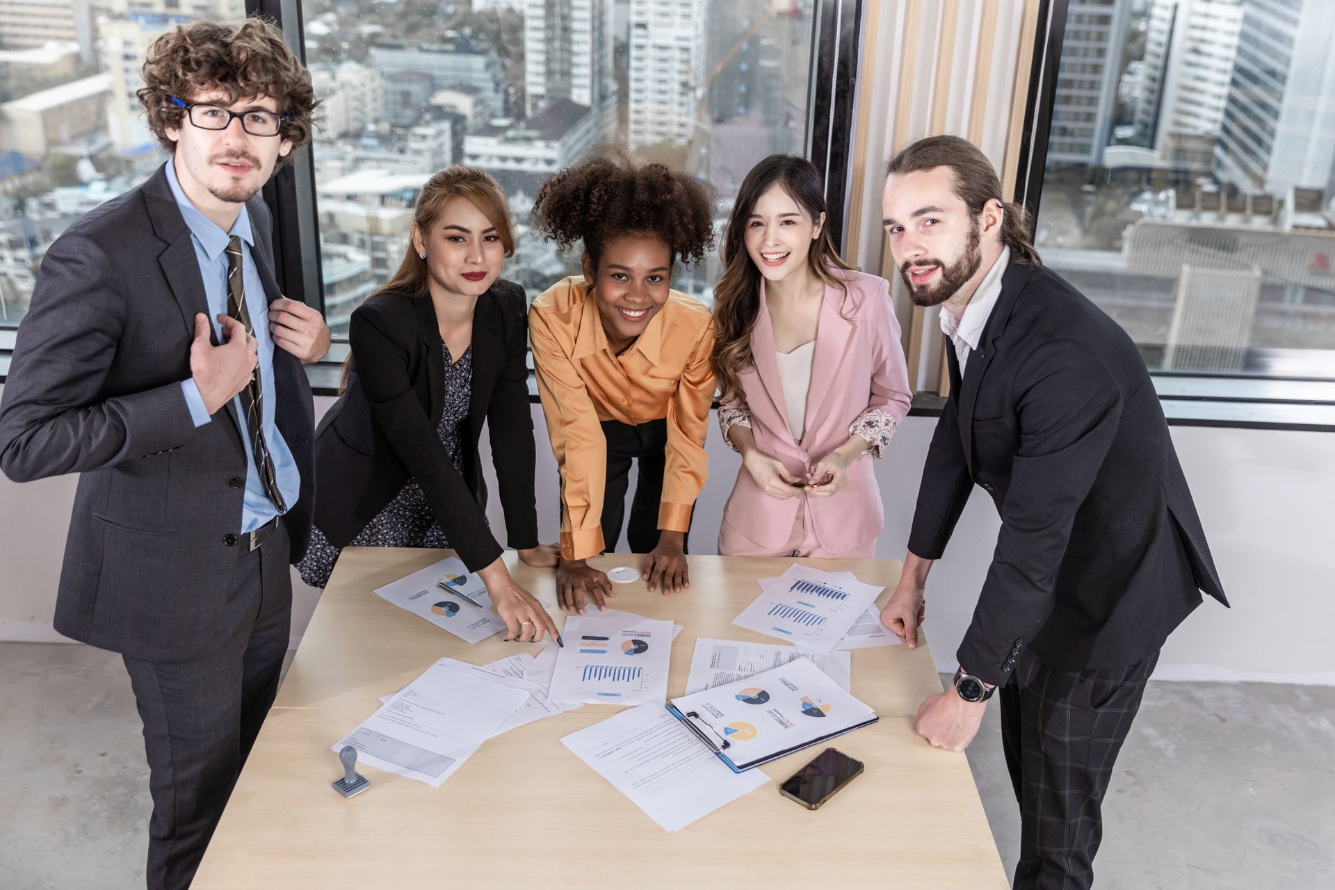 A group of business people are standing around a table with papers on it.