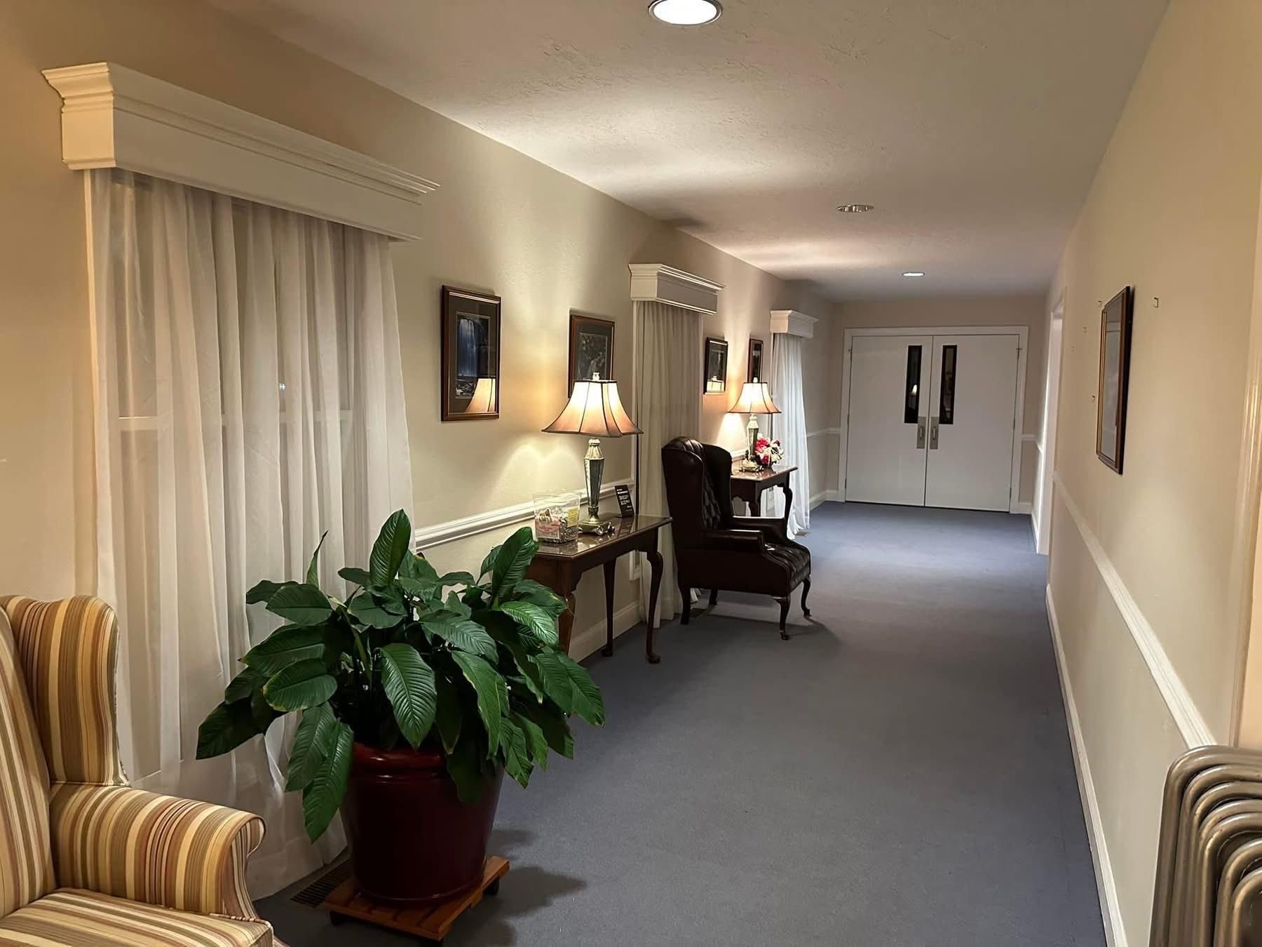 Hallway with seating, lamps, artwork, and large plant. Gray carpet and light walls.