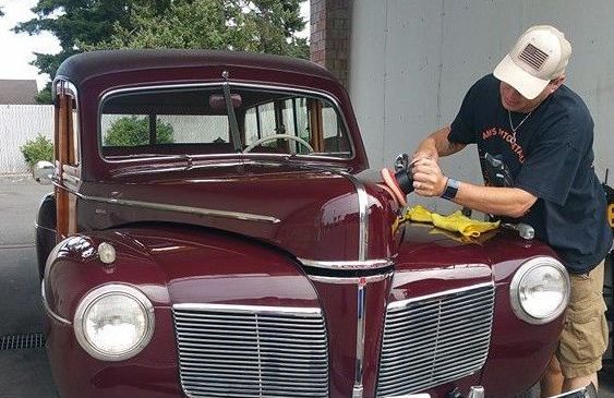 A man is polishing the hood of an old red car.