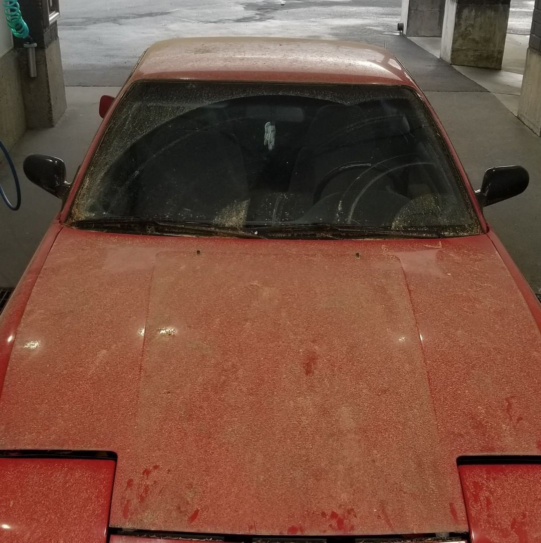 A dirty red car is parked in a parking lot