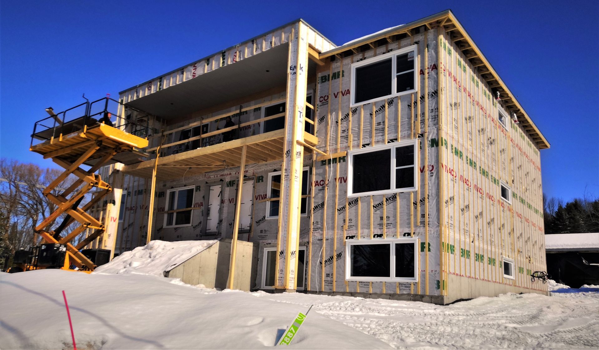 Maison à deux étages en construction sous la neige, avec des échafaudages et un ascenseur.