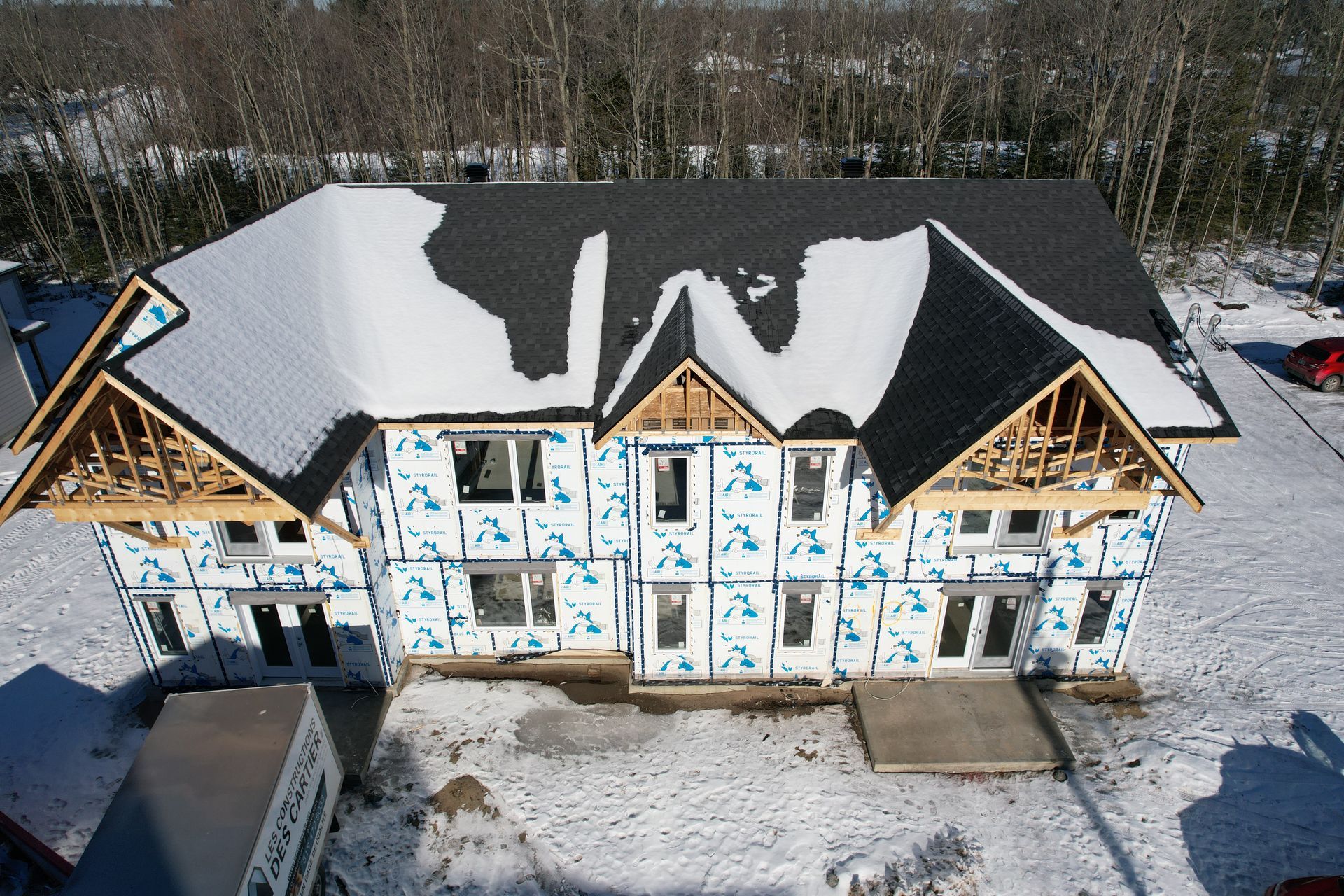 Construction d'une maison à deux étages avec une façade bleue et un toit enneigé, dans un environnement enneigé.