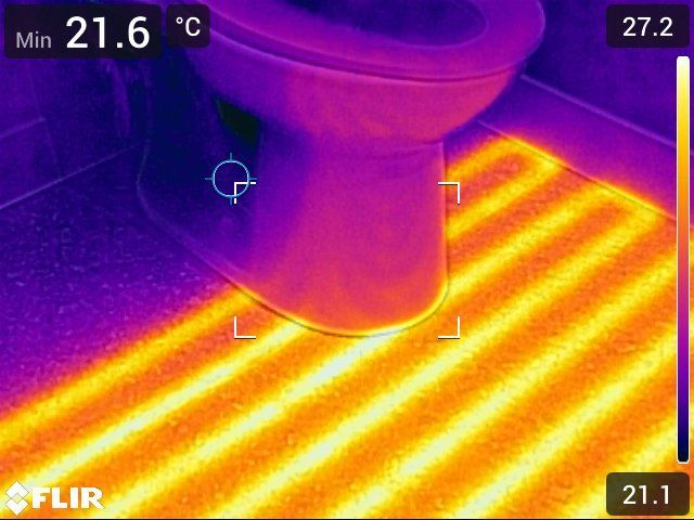 Image thermique de toilettes sur un sol chauffé, montrant des différences de température dans les tons orange et violet.