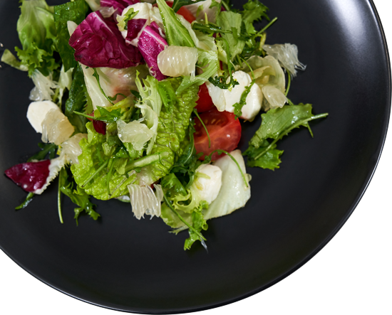 Salad with mixed greens, tomatoes, mozzarella, and grapefruit on a black plate.