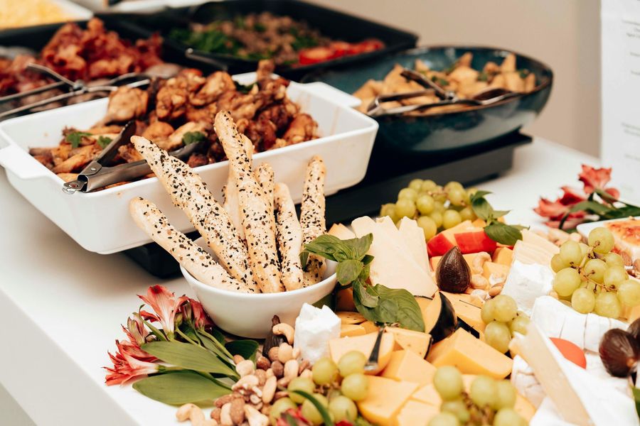 Buffet with various foods, including cheeses, grapes, breadsticks, and cooked dishes.