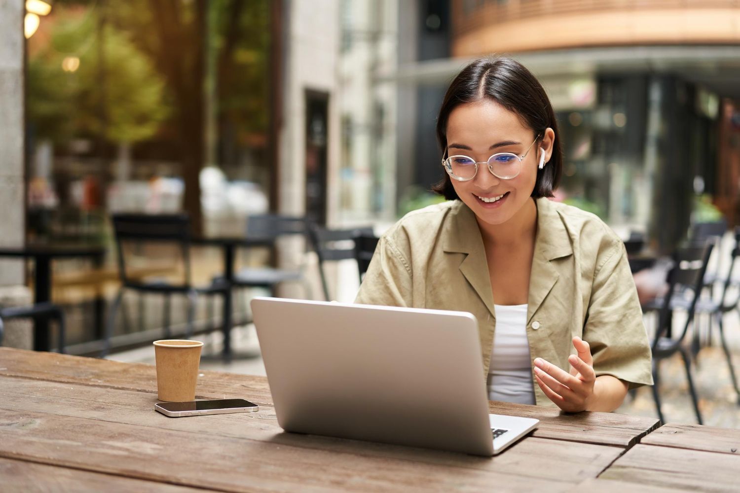 Person working on a laptop at an outdoor café table with a coffee cup nearby.