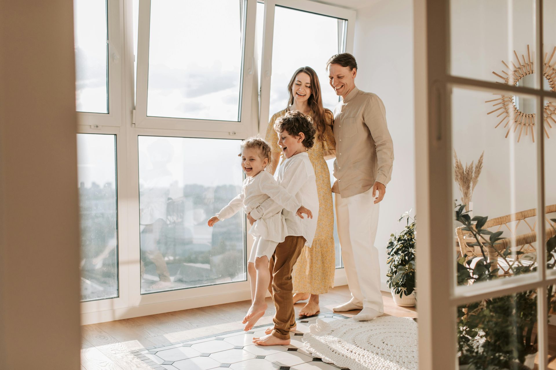 Family standing by sunlit windows in a bright living room, smiling and looking outside