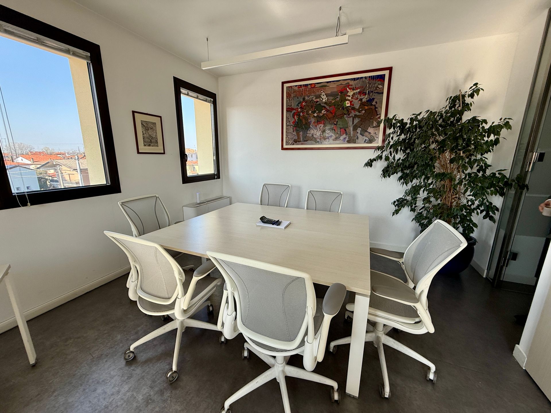 Una sala conferenze con un tavolo, delle sedie e un quadro alla parete.