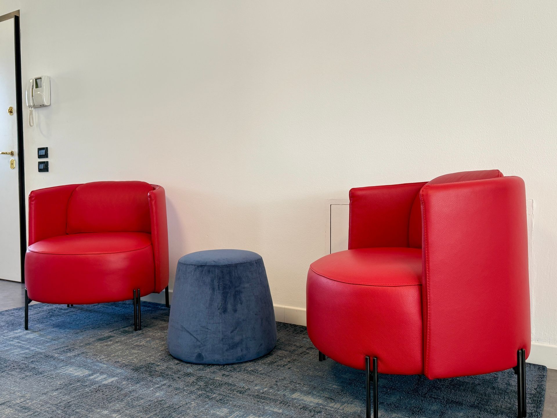 Due sedie rosse e un pouf blu sono posizionati uno accanto all'altro in una stanza.