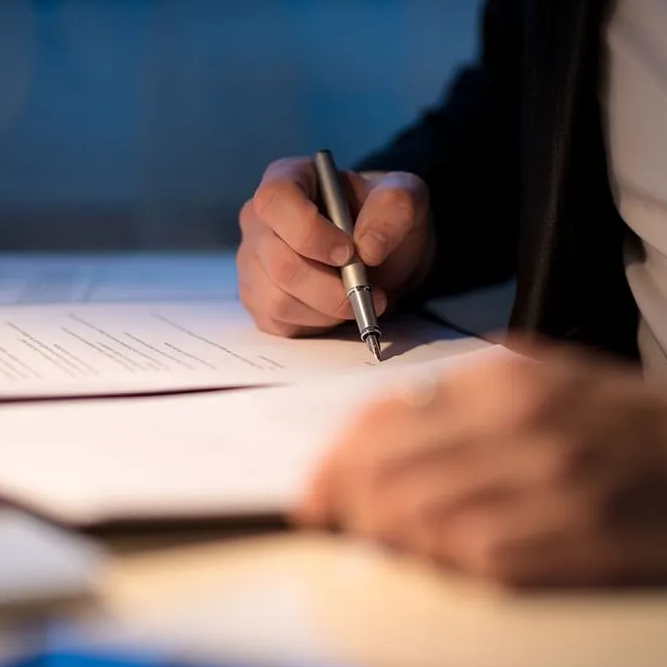 Close-up of a hand signing a document with a pen on a desk