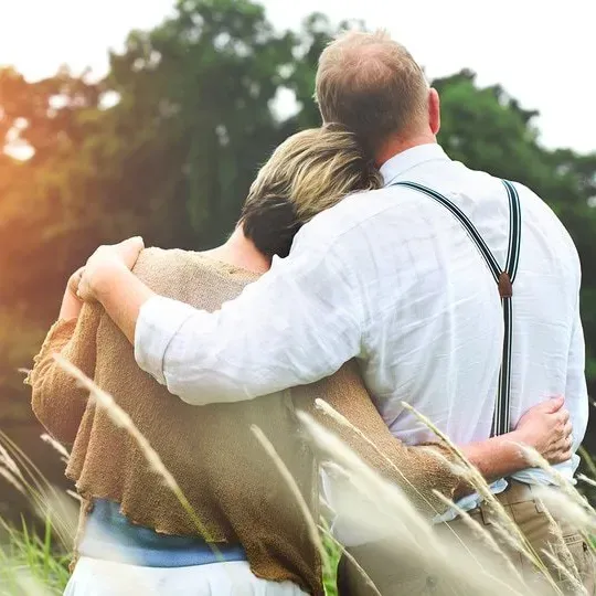 Two people embrace in a sunlit field, with tall grass and a blurred green background.