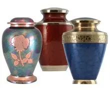 Three decorative urns with metallic lids, in blue, red, and floral-patterned pink enamel.