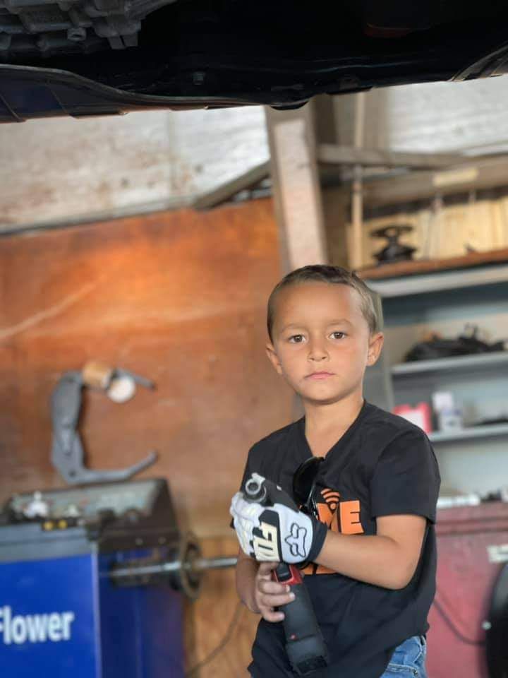 Boy in auto shop holding tool, looking at the camera.