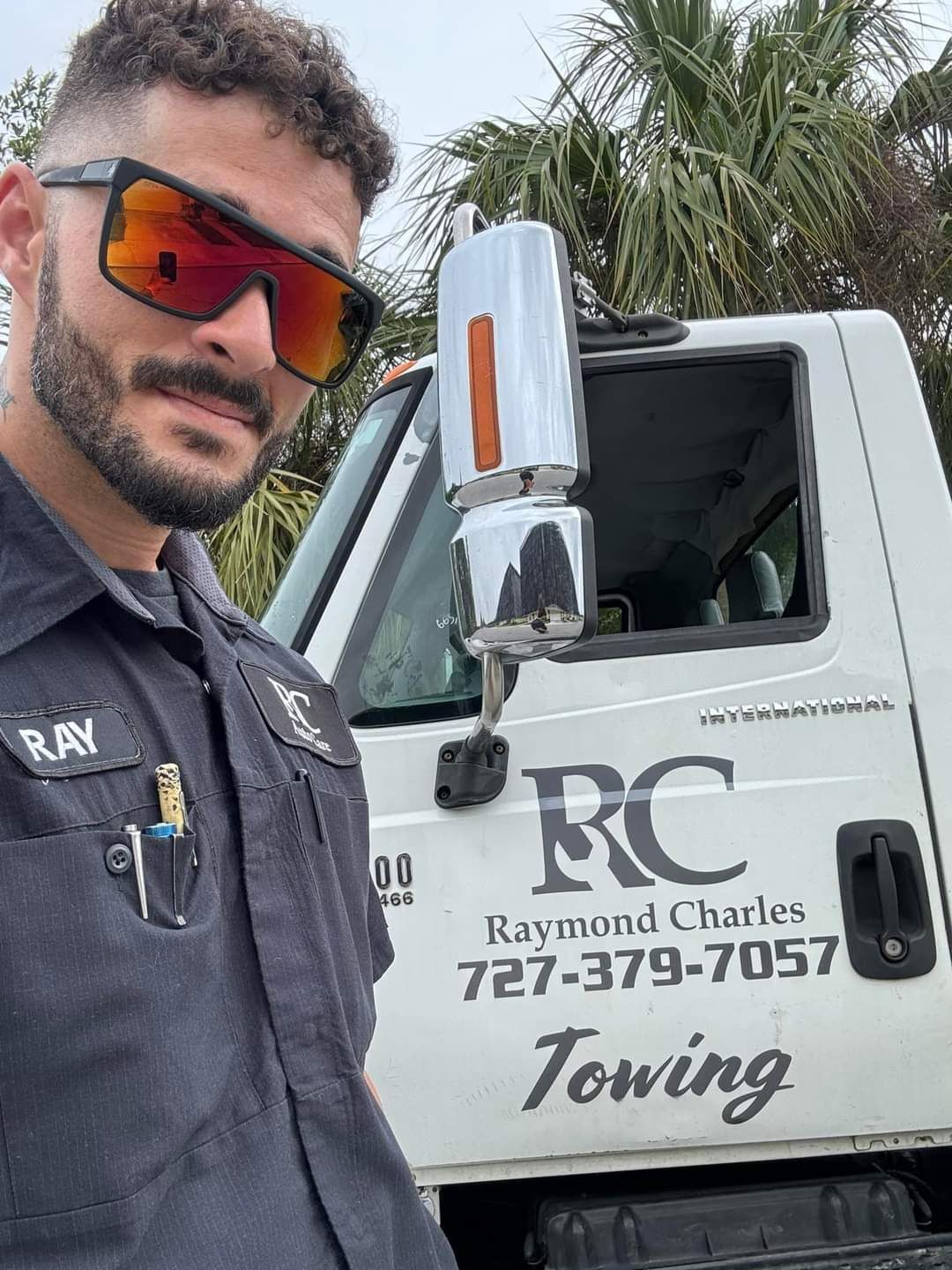 Man in uniform stands by RC Towing truck, wearing sunglasses.
