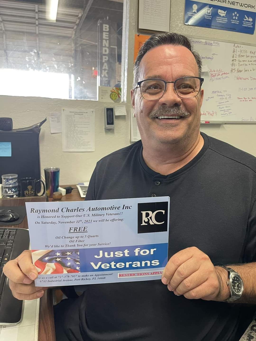 Man holding a "Just for Veterans" card with a military flag, smiling in an office.