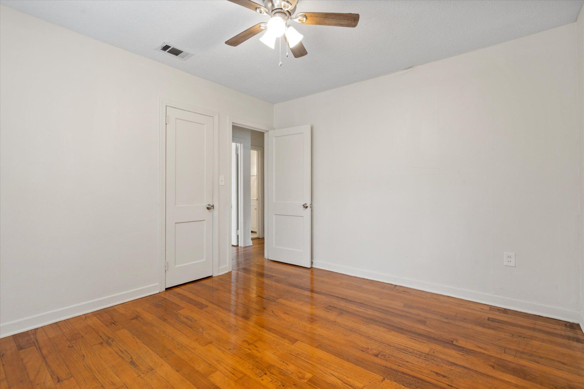 An empty bedroom with hardwood floors and a ceiling fan.