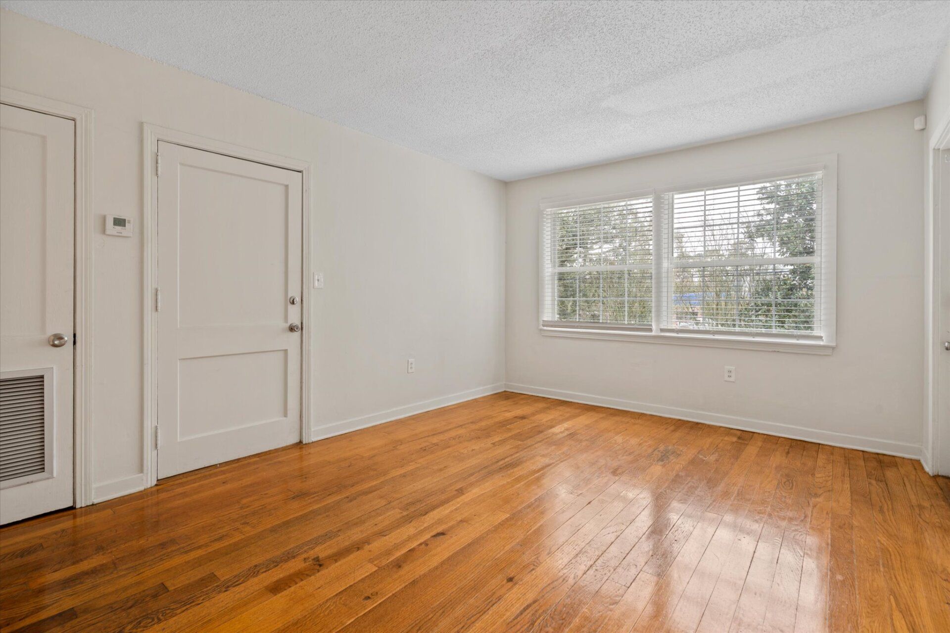 An empty living room with hardwood floors and white walls.
