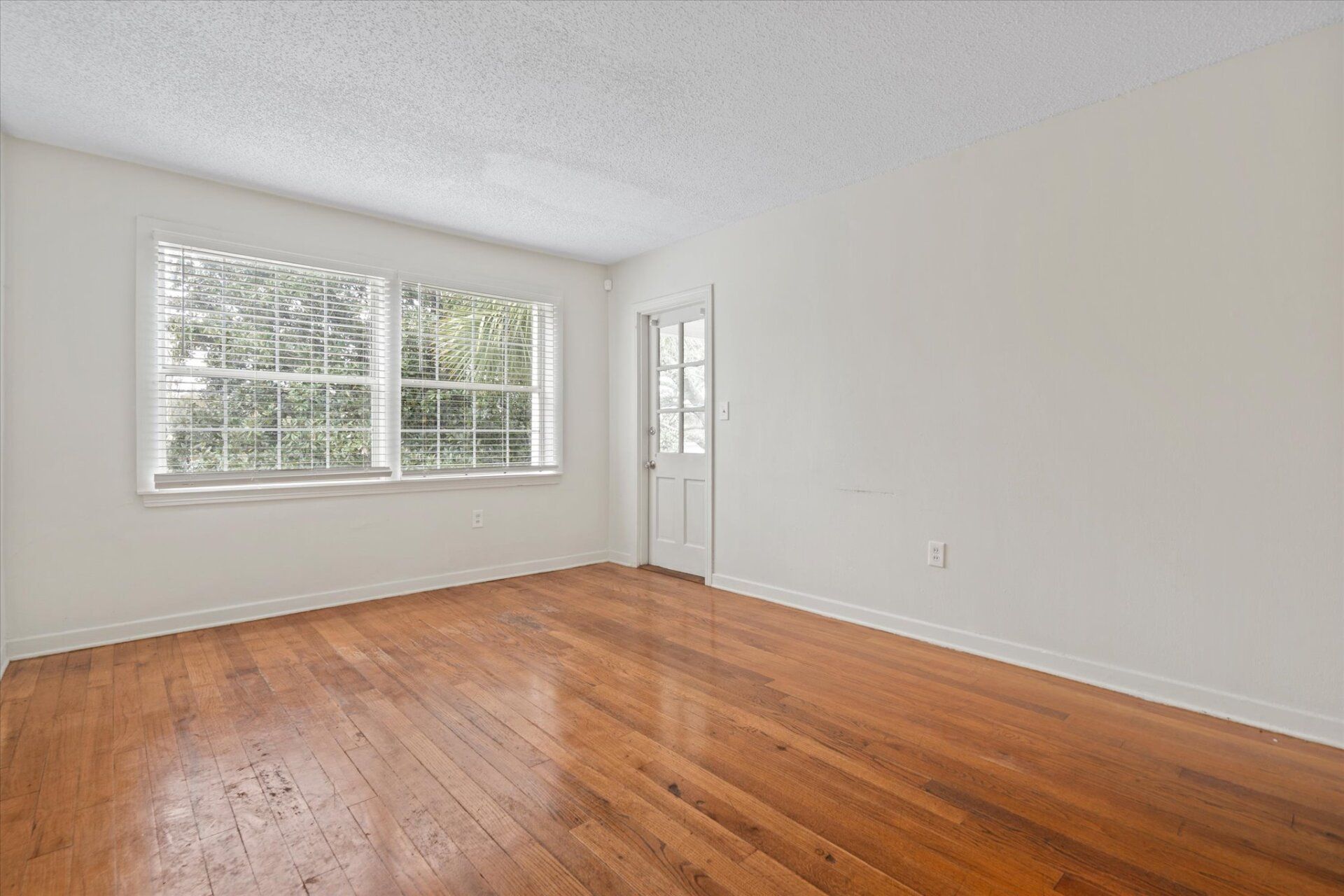 An empty living room with hardwood floors and two windows.