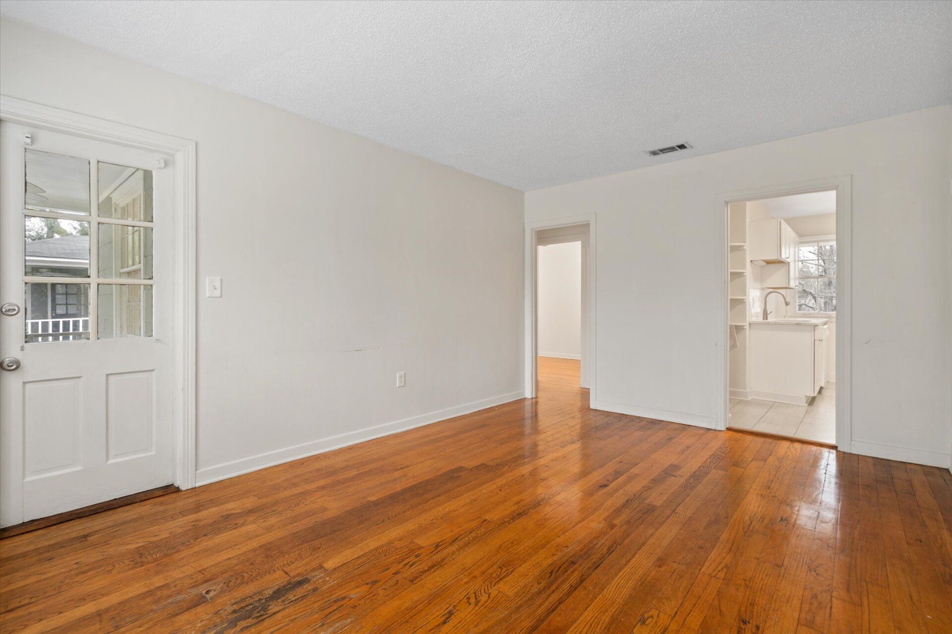 An empty living room with hardwood floors and white walls.