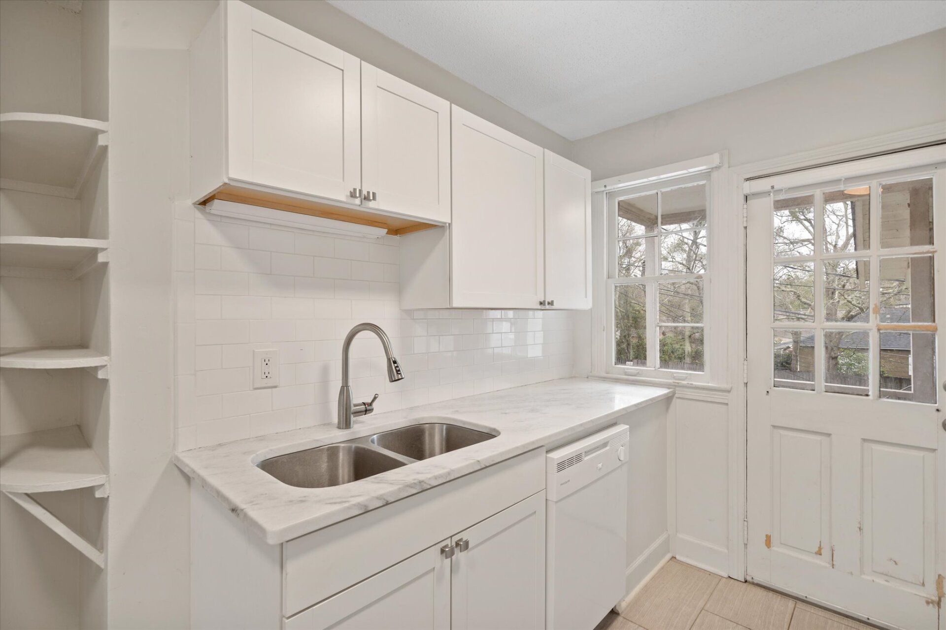 A kitchen with white cabinets , a sink , and a window.