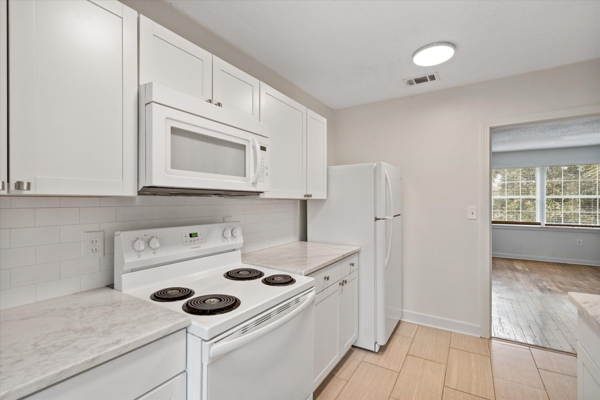 A kitchen with white cabinets , a stove , a refrigerator , and a microwave.