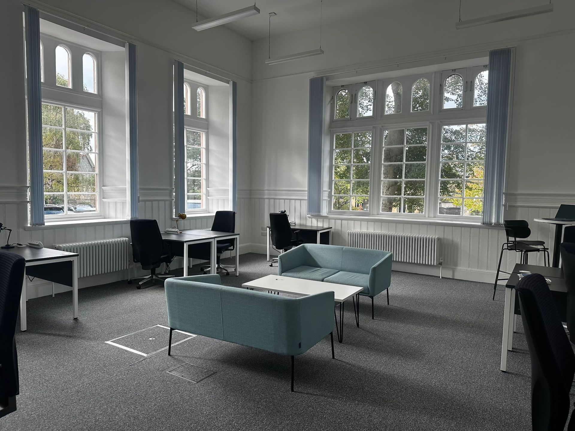 Bright room with large windows, light blue sofas, tables, chairs, and gray carpet.