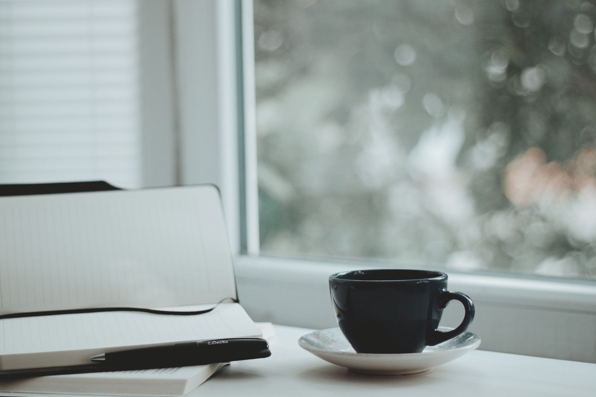 Notebook and coffee cup by a window, creating a calm space for reflection and life coaching.