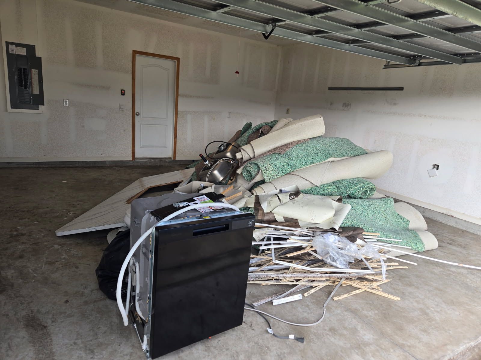 Garage interior with a pile of mattresses, chairs, and debris on the floor