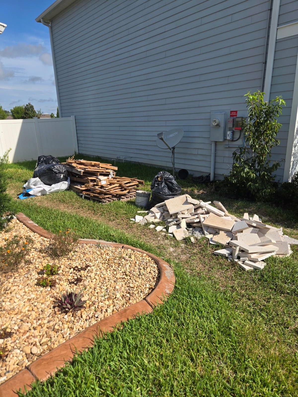 Yard beside a house with piles of broken tiles, wood, and debris near the wall.