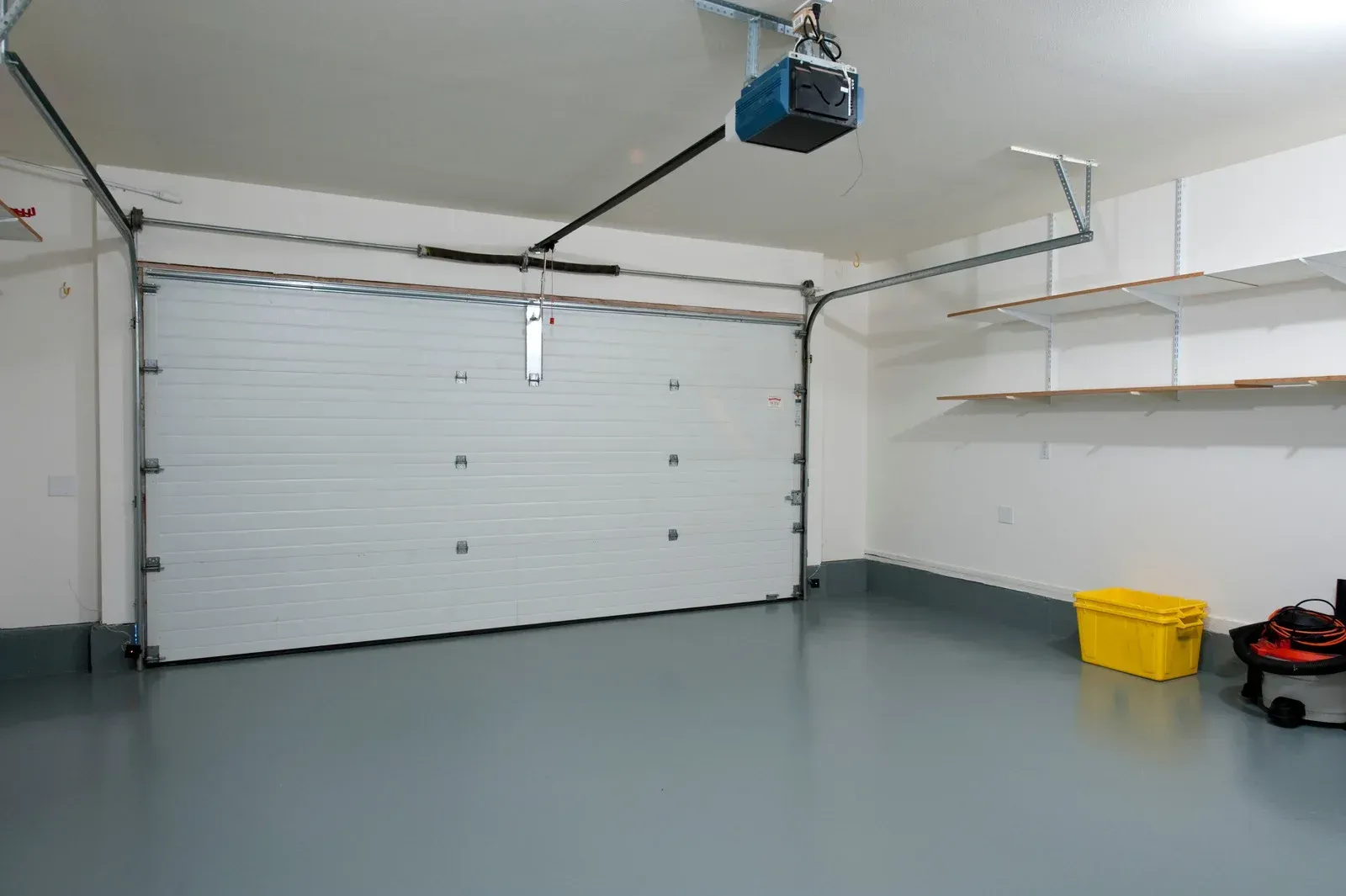 A garage with a white garage door and a blue garage door opener.
