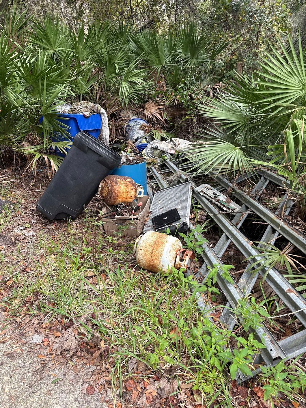A pile of trash is sitting on the side of a road in the woods.