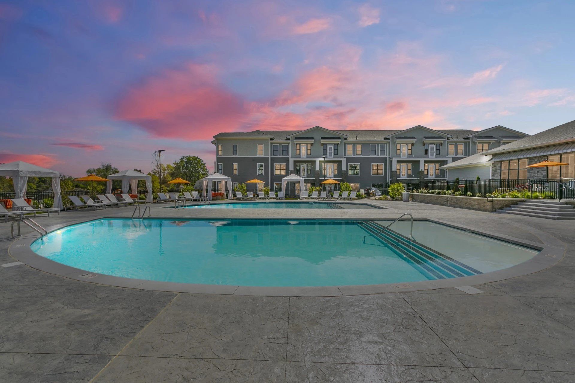 Outdoor hotel pool at dusk with lounge chairs and a modern building under a pink sky at Haven on Tucker Apartments in Louisville, KY.