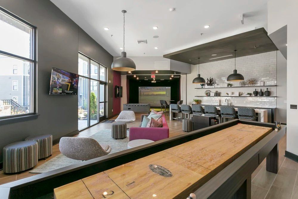 Modern loft lounge with pool table, seating area, and open kitchen in a bright industrial interior at Haven on Tucker Apartments in Louisville, KY.